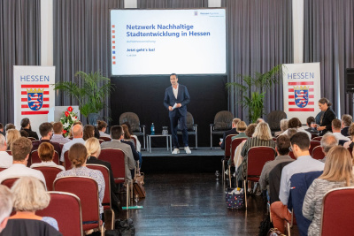 Moderator Daniel Fischer steht auf einer Bühne und redet.