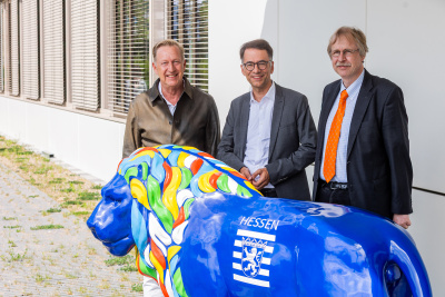 Folke Mühlhölzer, Christian Heinz und Alexander Bracht stehen vor einer großen, blauen Löwen-Statue vor einem Gebäude.