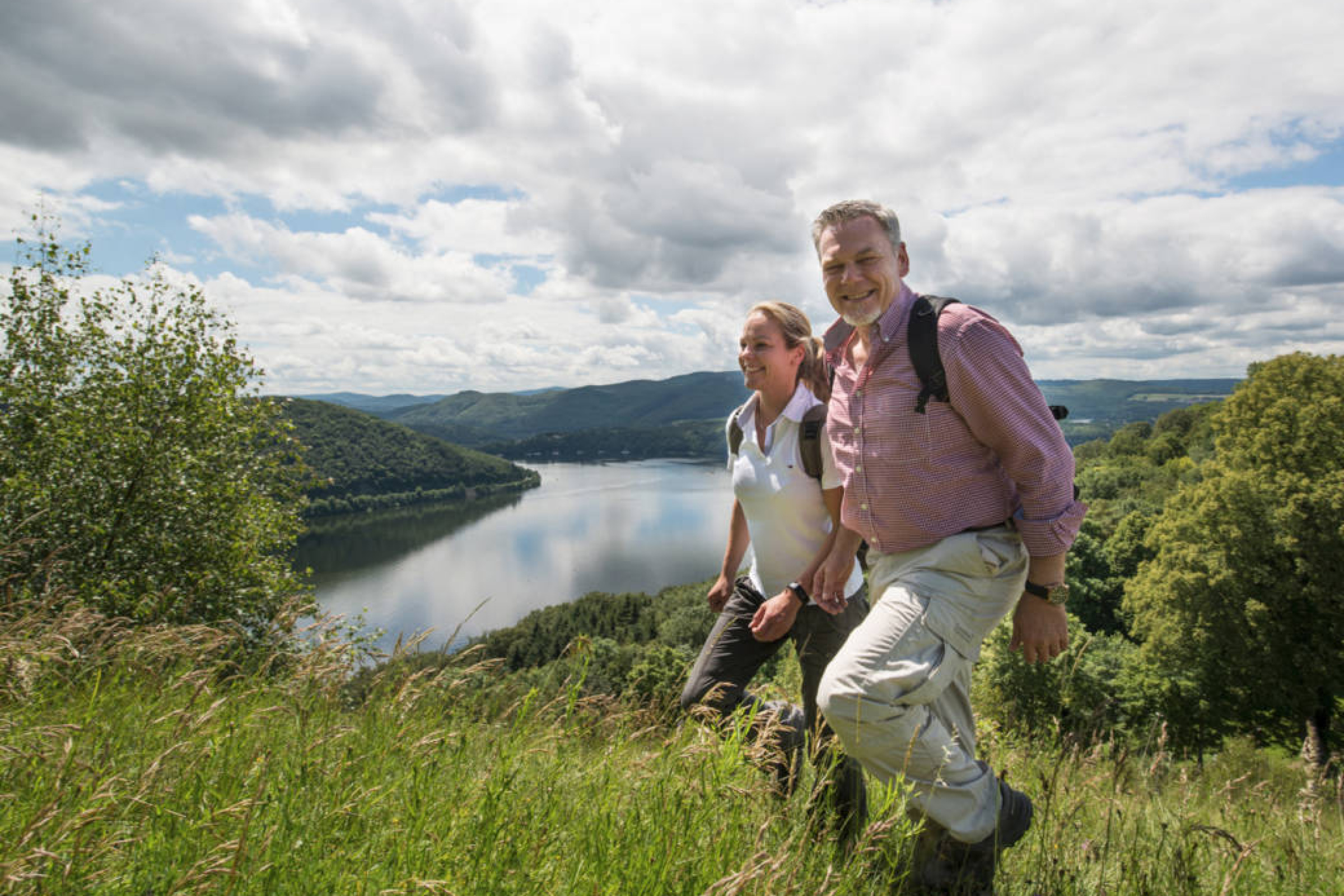 Wanderer, ein Frau und an Mann, laufen durch Gras vor dem Edersee.