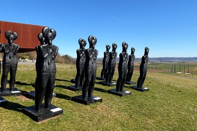 Mehrere Keltenfürstenskulpturen am Glauberg auf einer grünen Wiese. Das Museum Keltenwelt am Glauberg im Hintergrund leicht sichtbar.